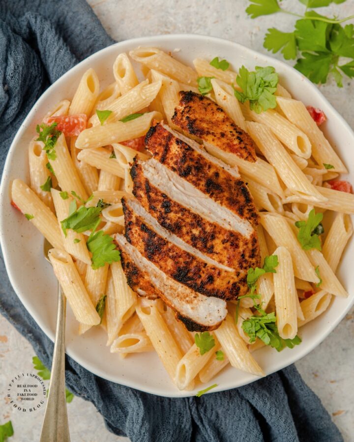 Blackened Chicken with dry rub spices charred on top of a bed of penne pasta in a bowl with olive oil, parmesan cheese and tomatoes #blackenedchicken #cajunchicken #lowcarb #ketofriendly #whole30 #paleo #glutenfree