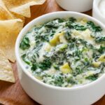 bowl of spinach artichoke dip on cutting board with tortilla chips