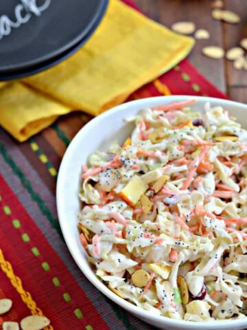 white bowl of coleslaw with apples, cranberries and almonds on festive placemat