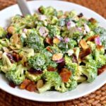 white plate with crisp fresh broccoli, slivered almonds, red onion, bacon in dressing