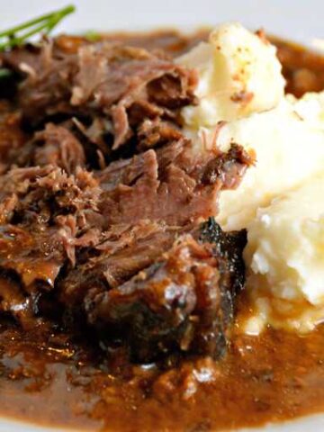 white plate with slow cooker pot roast, gravy and mashed potatoes
