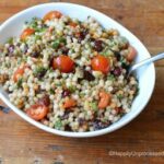 Overhead shot of Israeli couscous, grape tomatoes in white bowl with spoon