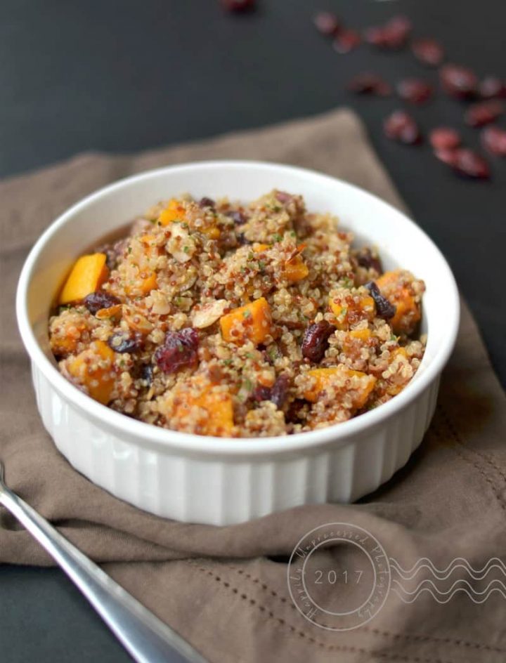Roasted butternut squash with quinoa, dried cranberries, toasted almonds in white bowl with brown napkin