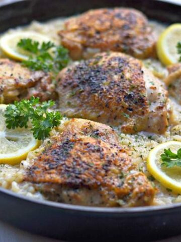 Large cast iron skillet chicken thighs lemon pepper risotto garnished with lemons
