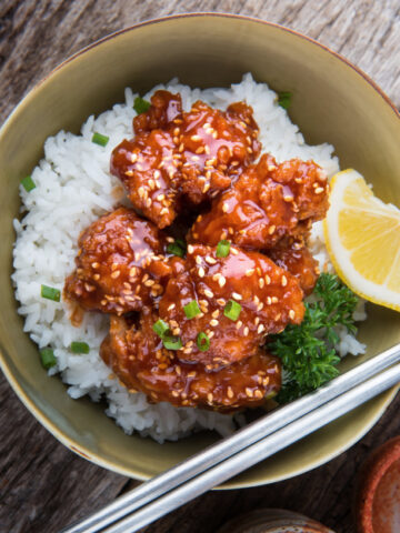 sesame chicken with toasted sesame seeds over white rice in a bowl