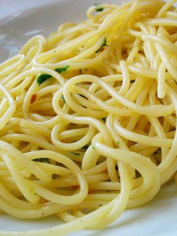 white plate with fluffy spagetti aglio e olio, red pepper flakes and parsely