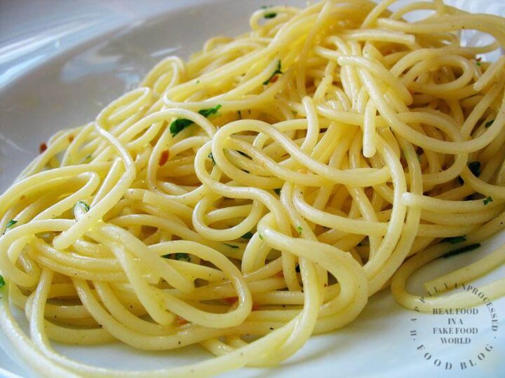 white plate with fluffy spagetti aglio e olio, red pepper flakes and parsely