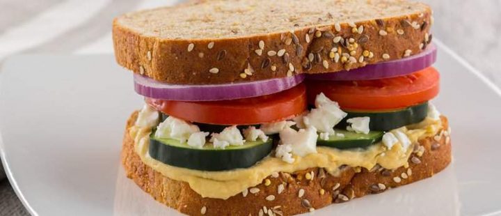veggie sandwich with onion, tomato, cucumber, feta cheese and roasted red pepper hummus on whole wheat bread