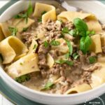 Hamburger Helper Beef Stroganoff in a white bowl with large egg noodles and garnished with parsley