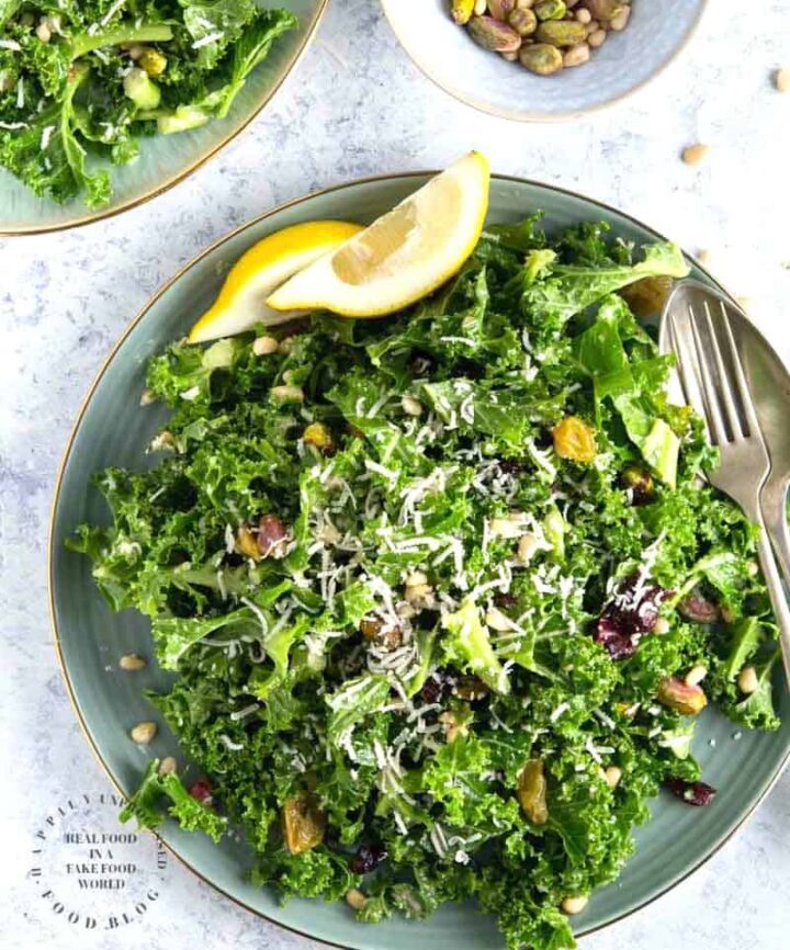 An easy lemony garlic kale salad with pistachios, pine nuts, dried cranberries topped with shaved parmesan cheese #newyearsresolution #kale #salad #healthy #happilyunprocessed