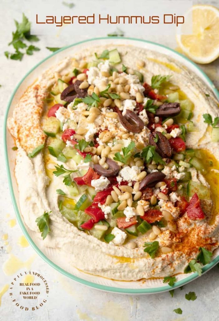 LAYERED HUMMUS DIP - Homemeade Hummus topped with Kalamata olives, cucumbers, roasted red peppers, feta cheese and pine nuts #hummus #healthy #chickpeas #tahini #happilyunprocessed