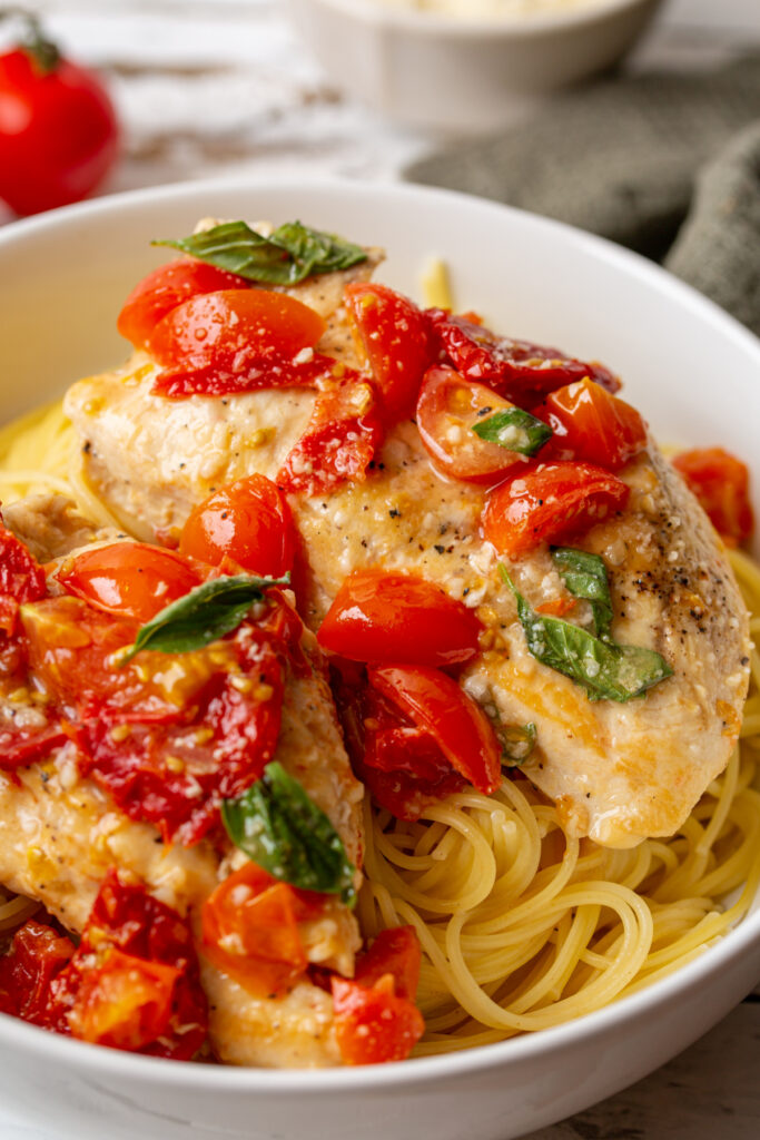 Tomato Basil Chicken in a Garlic and butter sauce over garlic butter angel hair pasta in a white bowl