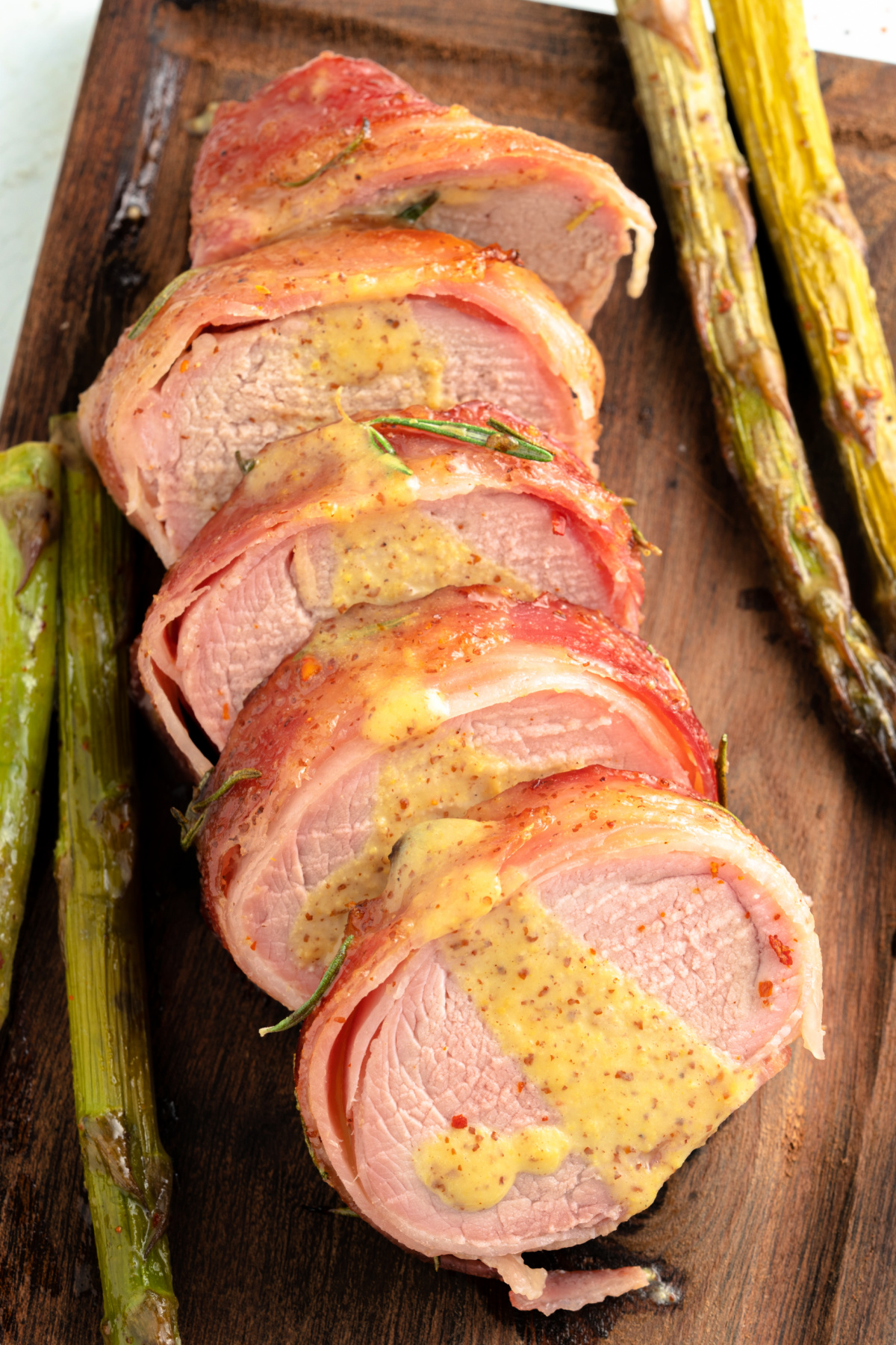 Bacon Wrapped Pork Tenderloin sliced on a cutting board drizzled in a honey dijon sauce