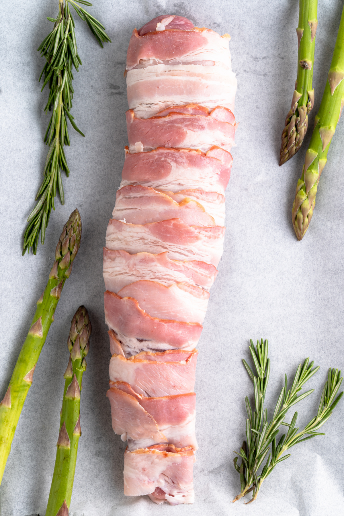 A pork tenderloin completely wrapped in bacon prior to cooking