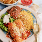 Traditional Mexican chicken enchiladas dinner served with rice and refried pinto beans