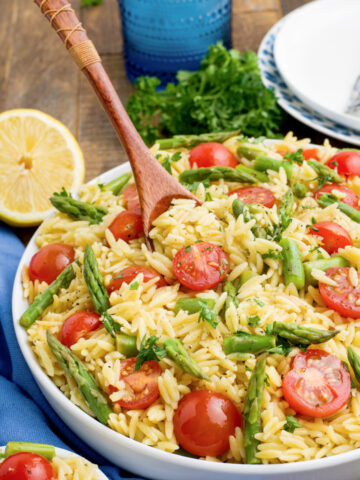 Lemon Orzo with tomatoes and asparagus with a wooden spoon in a large bowl