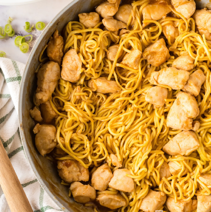 Garlic and ginger Chicken and chow mein noodles in a hot skillet garnished with scallions.
