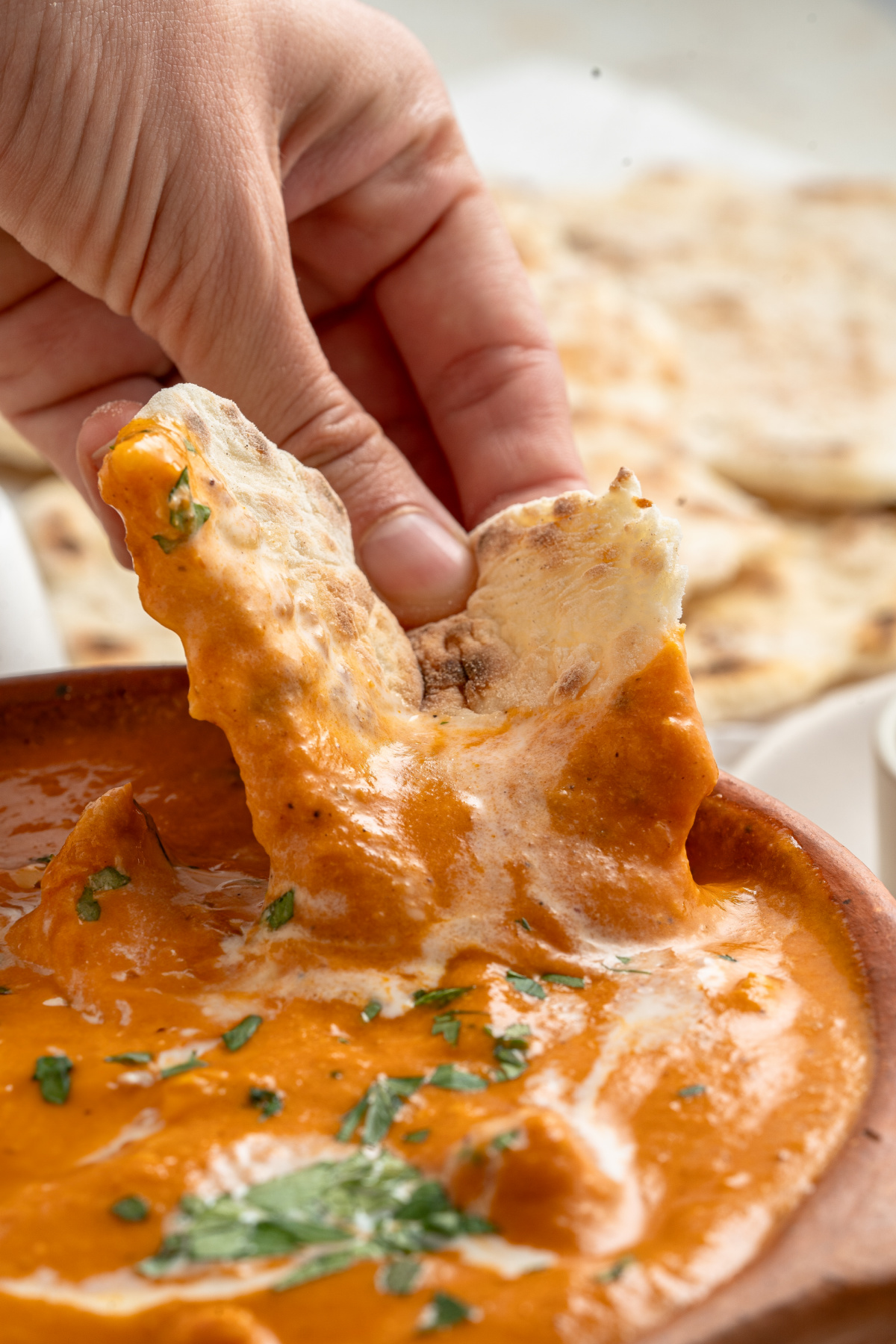 Warm naan bread being dipped in homemade Chicken Makhani (butter chicken) sauce with chicken