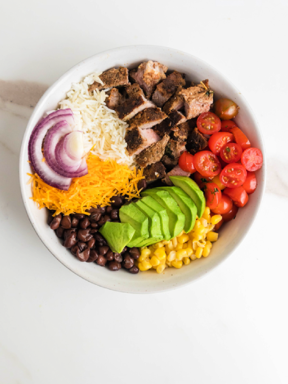 a steak burrito bowl with brown rice, tomatoes, red onions, shredded cheese